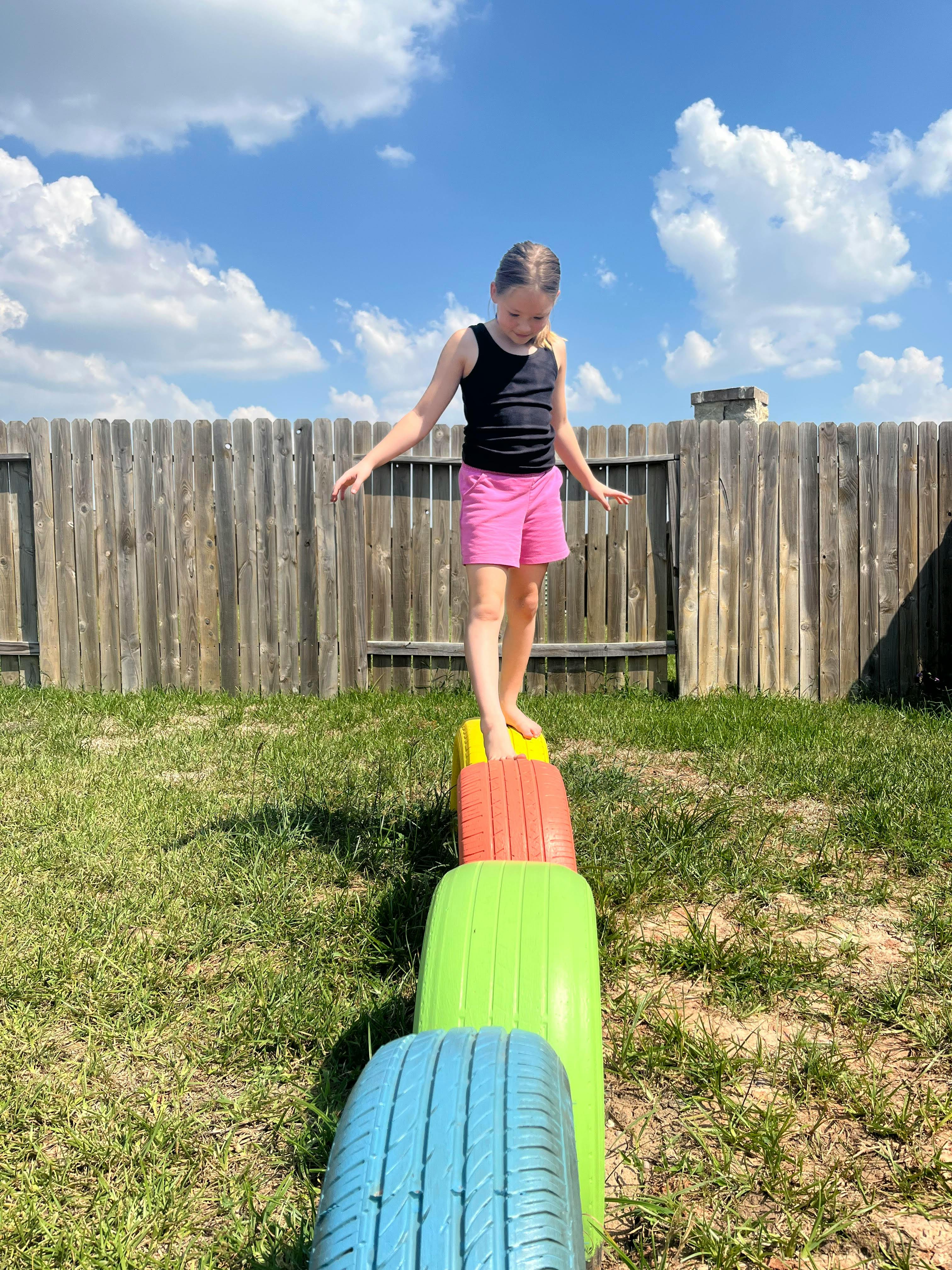 Child balancing on colorful tires in a grassy yard