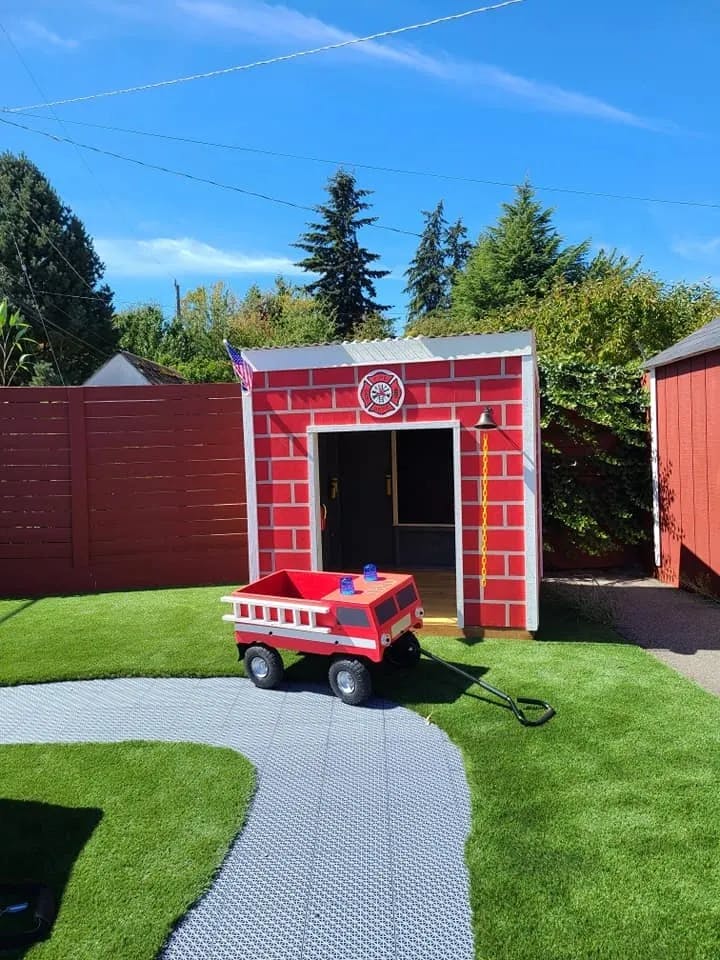 Red toy fire truck in front of a small red brick playhouse