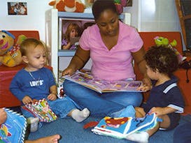 Adult reading a book to two children in a classroom