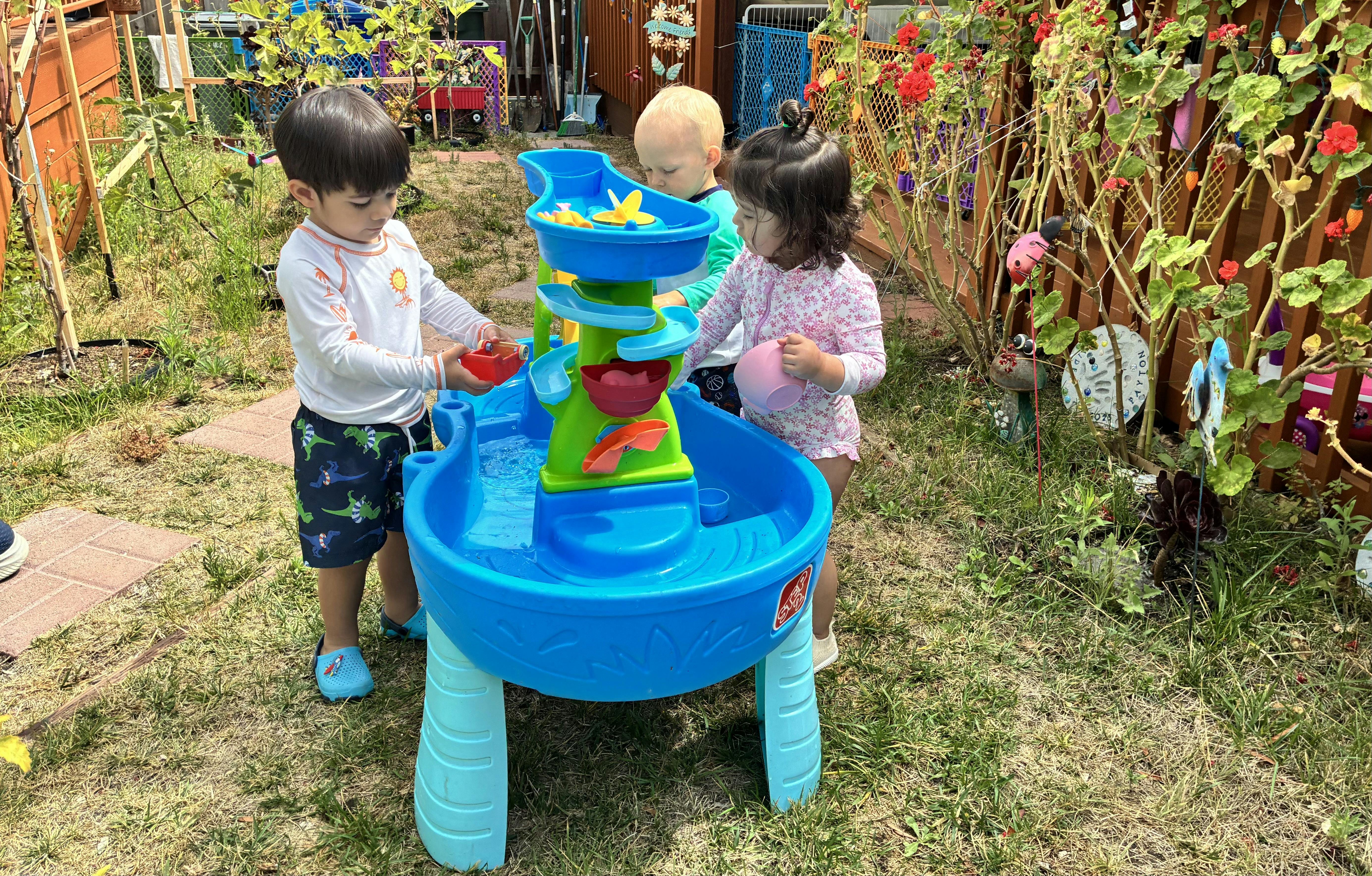 Three children playing with a water table in a backyard