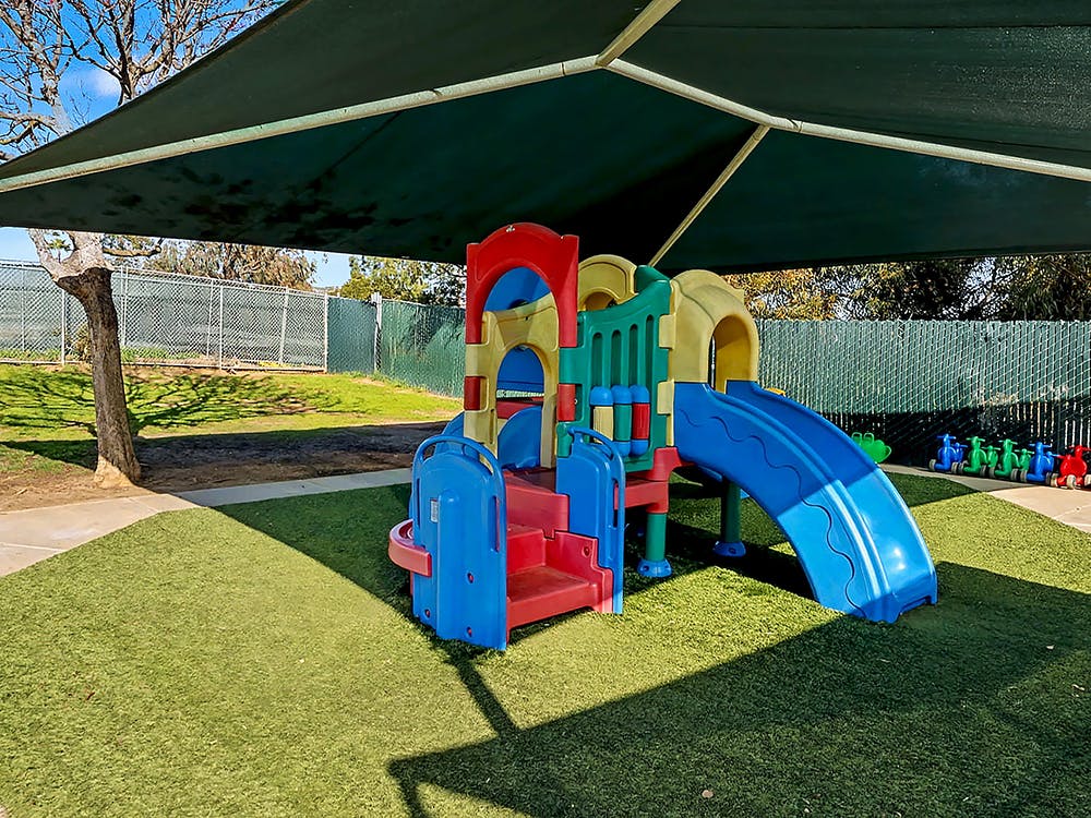Colorful playground structure with a blue slide on artificial turf under a shade canopy