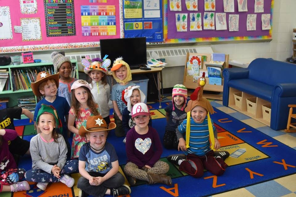 Group of children wearing hats sitting on a colorful rug in a classroom