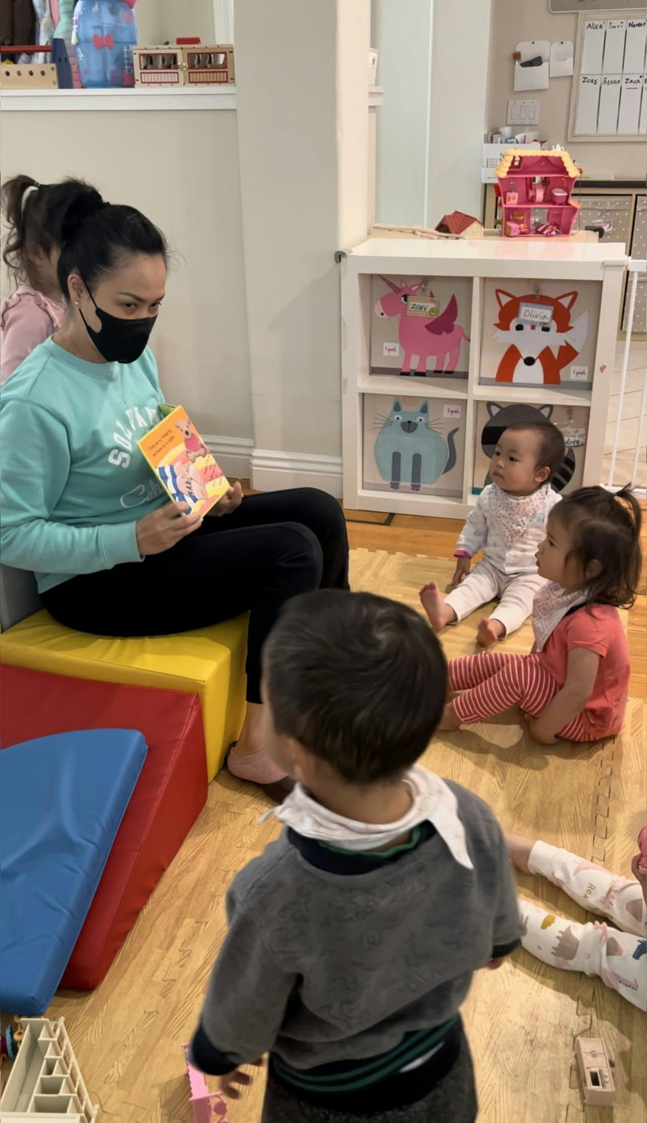 Person in mask reading a book to children in a classroom