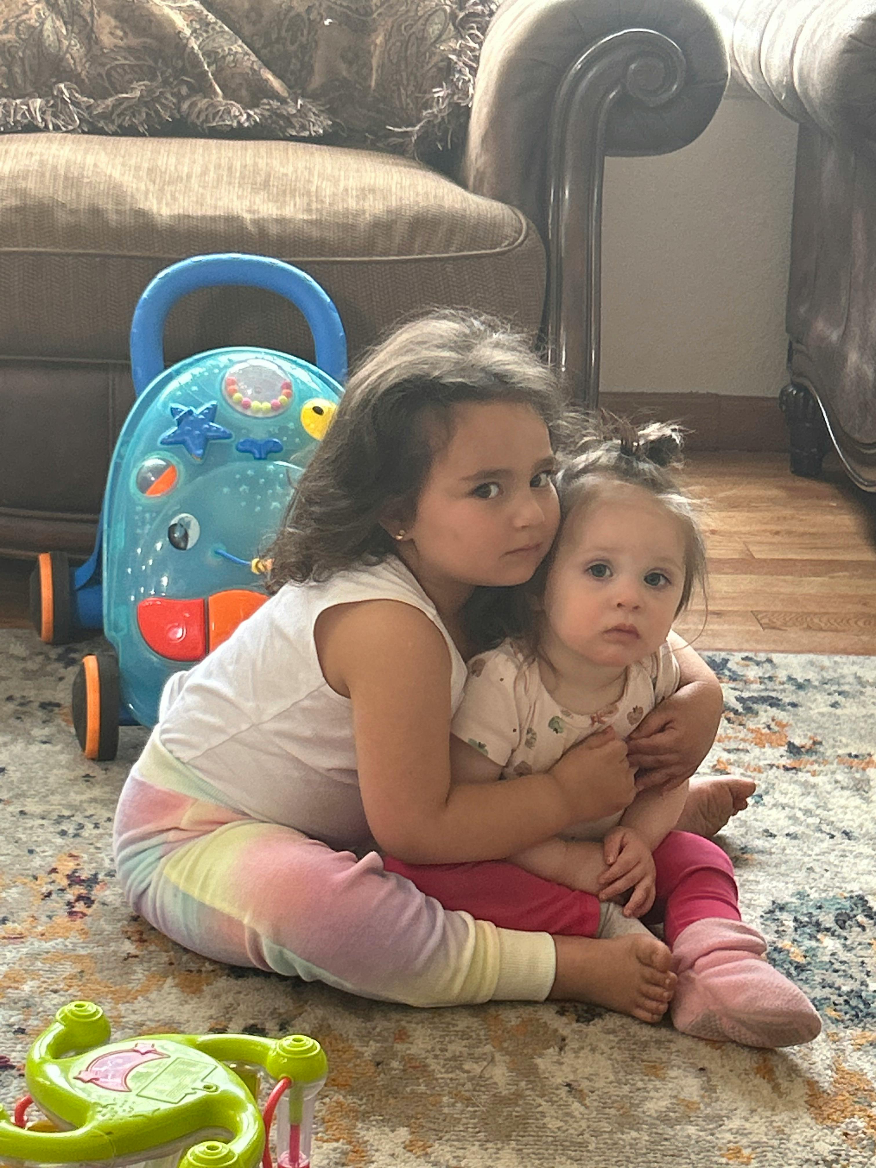Child embracing a younger child on a rug