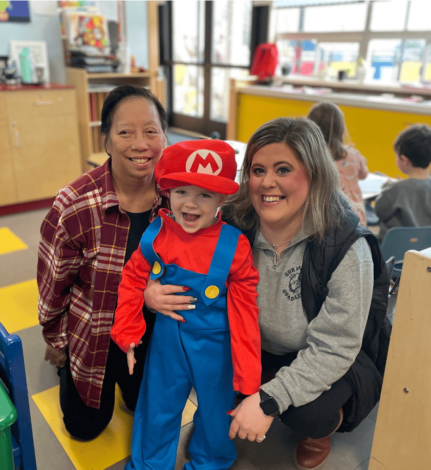 Child dressed as Mario with two adults in a classroom