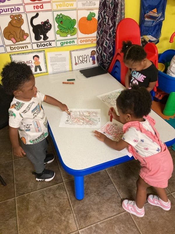 Three children coloring at a small table in a classroom