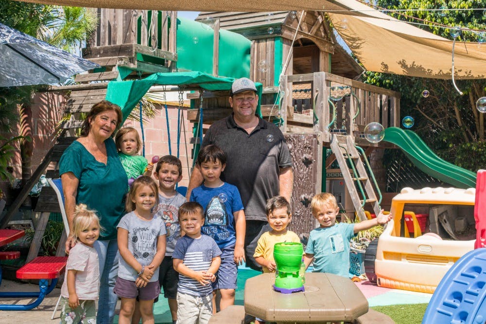 Two adults and multiple children standing in front of a playground structure