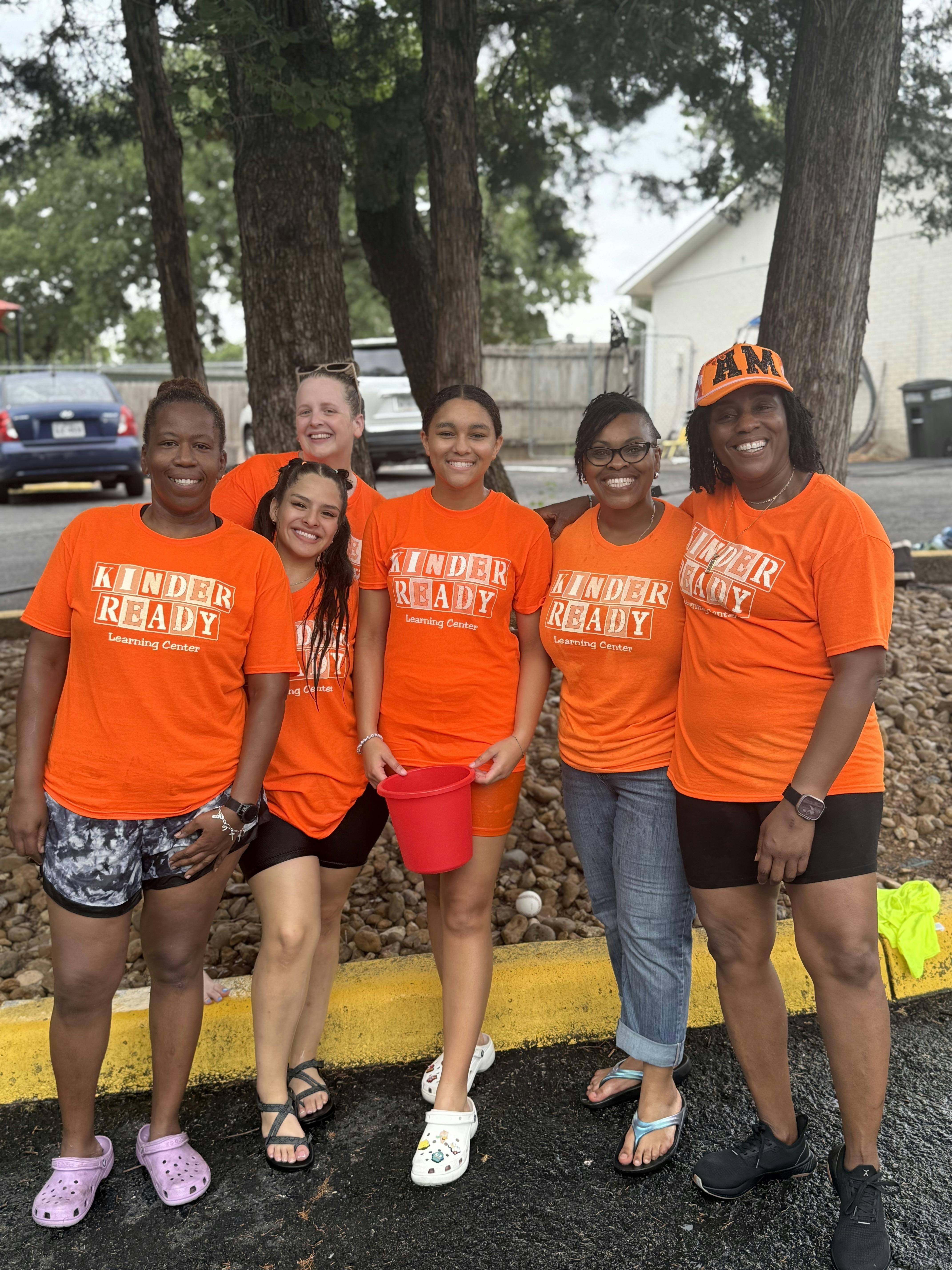 Six people in orange shirts with "Kinder Ready" text, one holding a red bucket