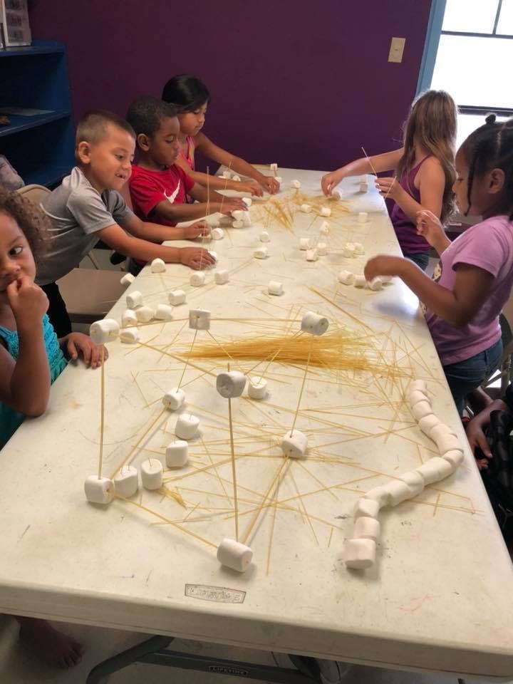 Children building structures with marshmallows and spaghetti noodles on a table