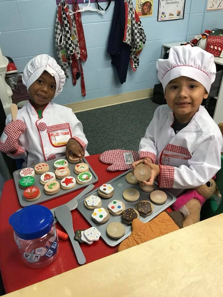 Two children in chef hats and coats with trays of play cookies