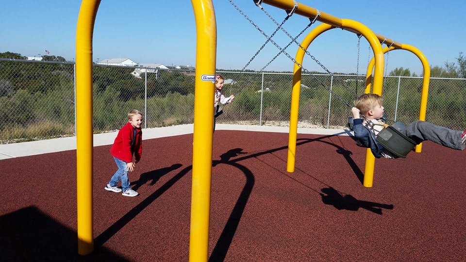 Child on a swing set with another child standing nearby