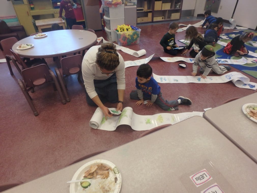 Adult and child on floor with long paper scroll in classroom