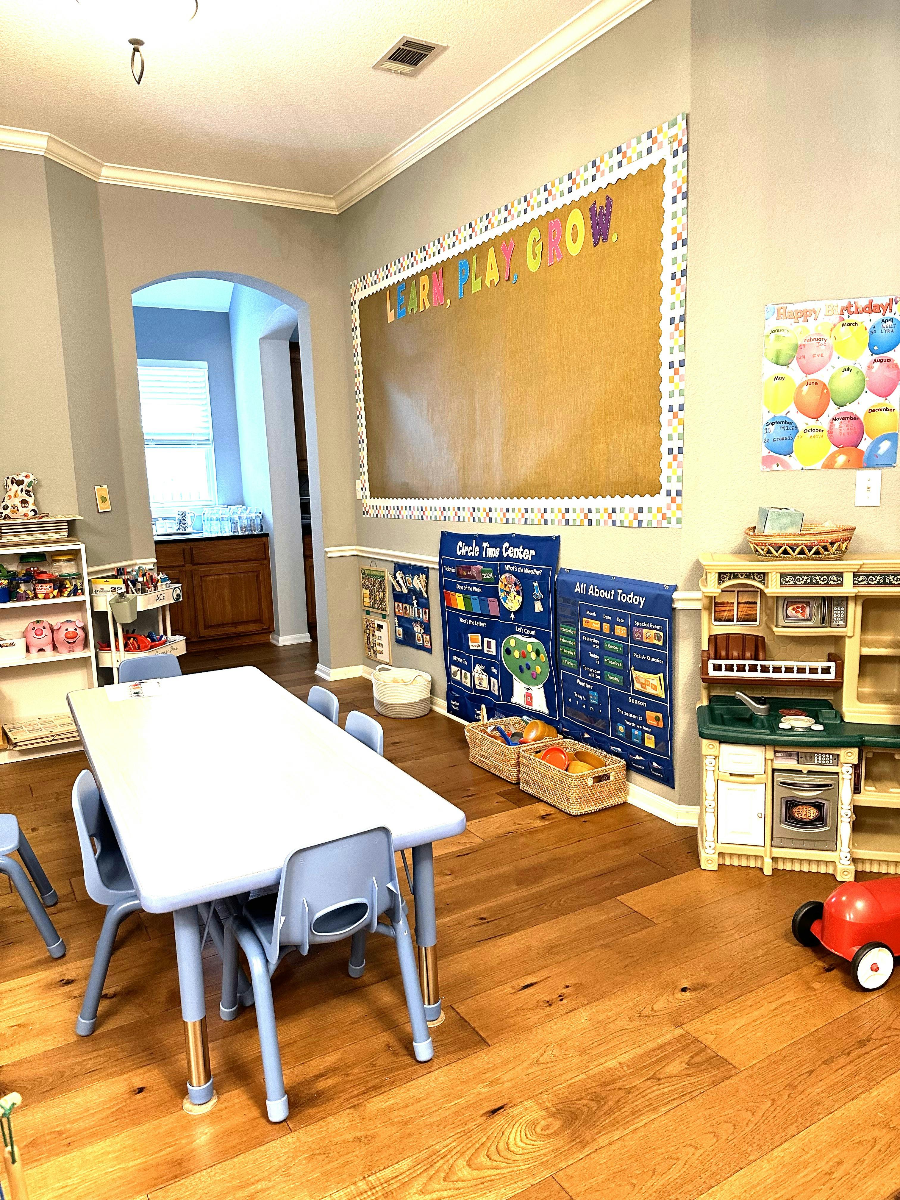 Classroom with a table and chairs, play kitchen, and bulletin board