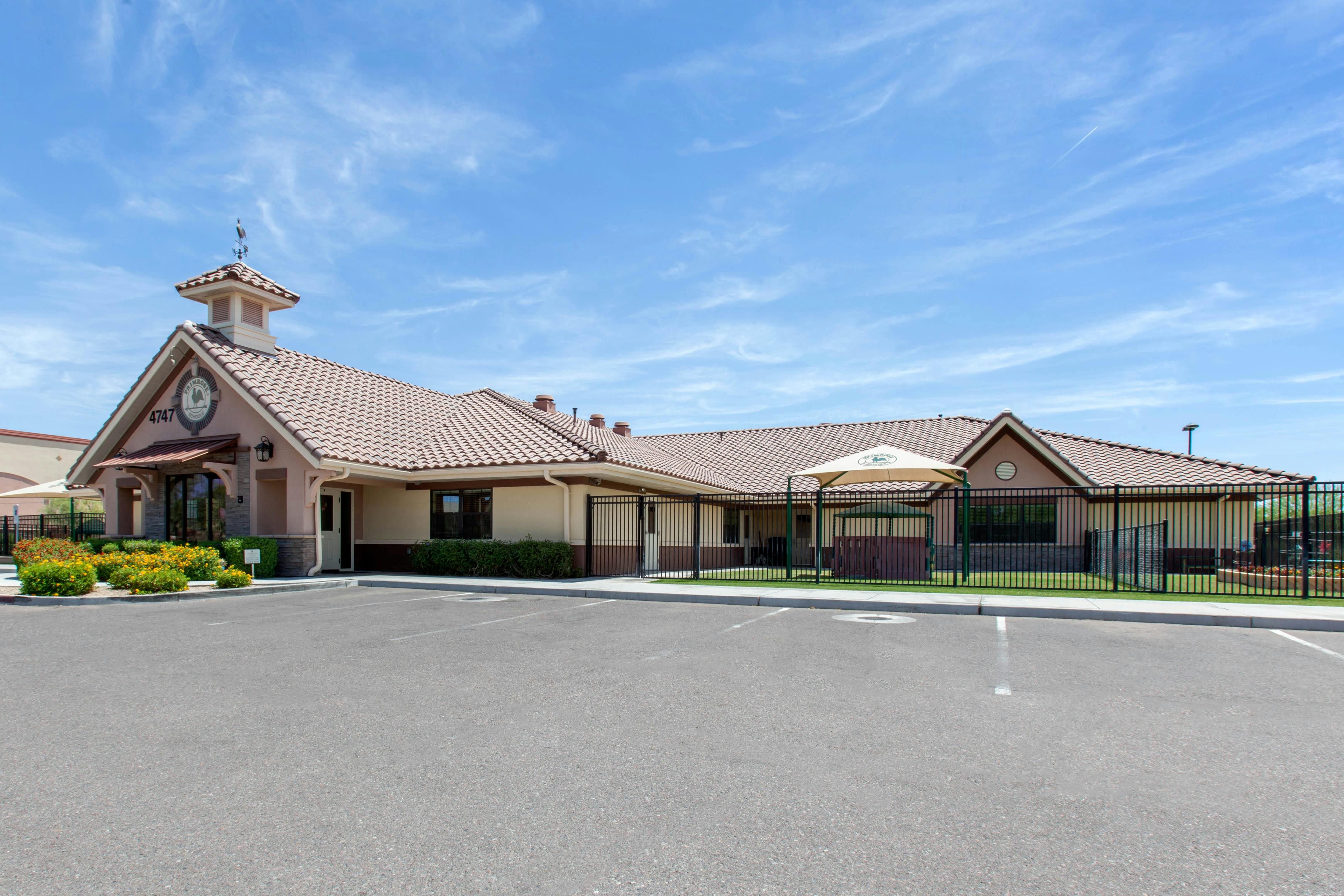 A beige building with a tiled roof and small steeple over the entrance, seen from a parking lot