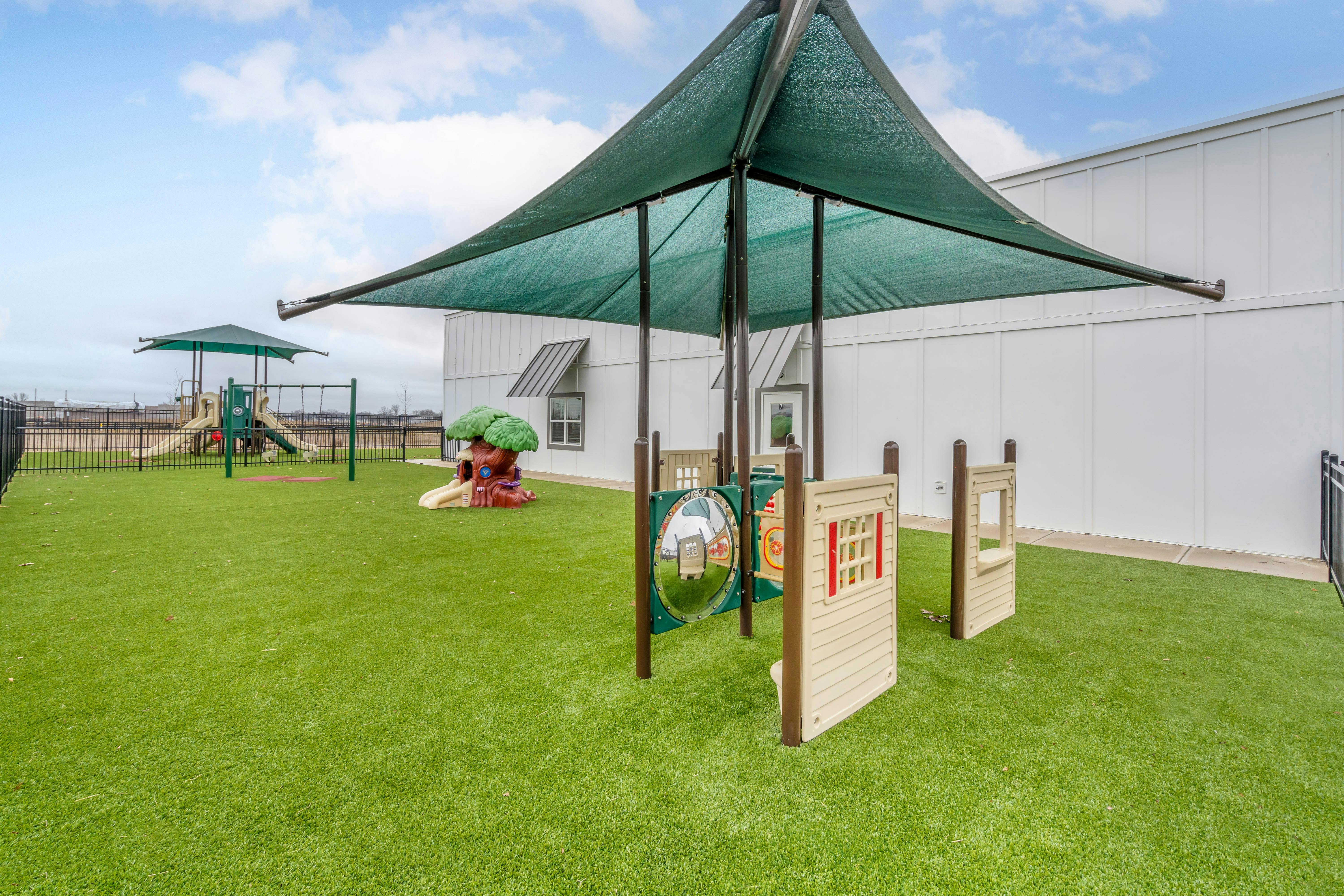 Playground area with artificial turf, shade structure, and various play equipment