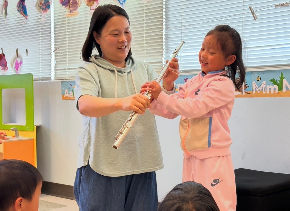 Person helping a child assemble a flute in a classroom