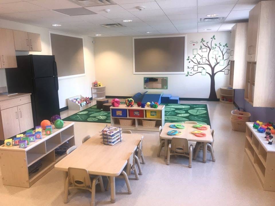 Playroom with small tables and chairs, toys, and a tree mural on the wall