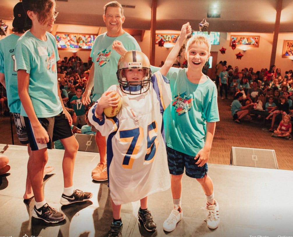 Child in oversized football uniform holding a football next to another child