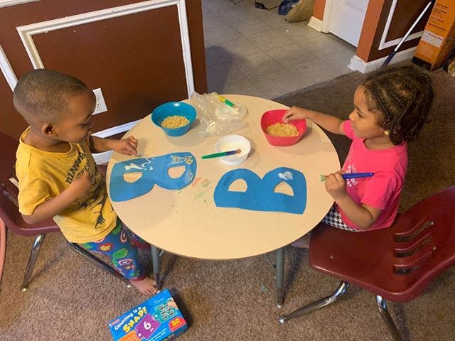 Two children at a table with craft supplies and blue paper masks