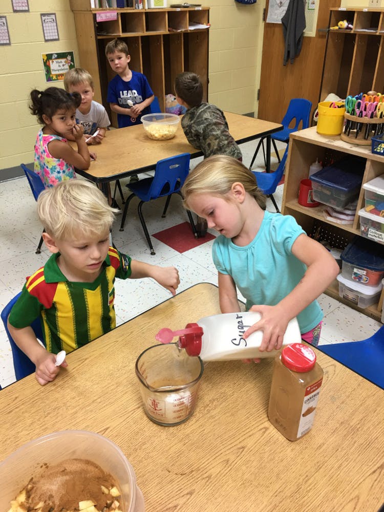 Child pouring sugar into a measuring cup, another child watching