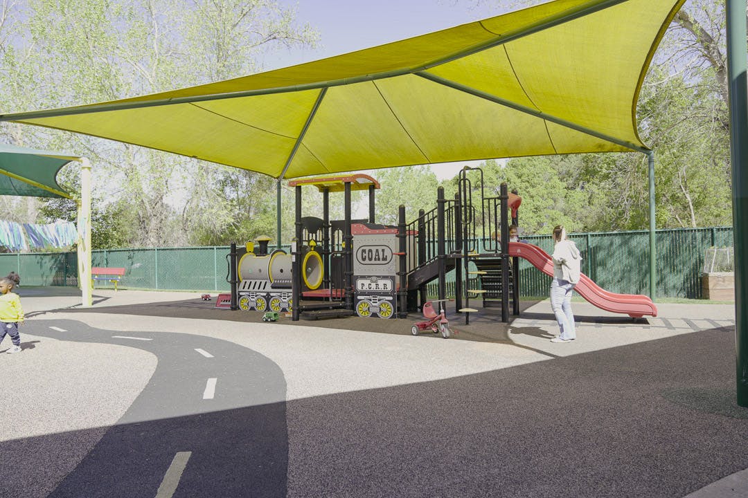 Playground with yellow shade structure, play equipment, and two people