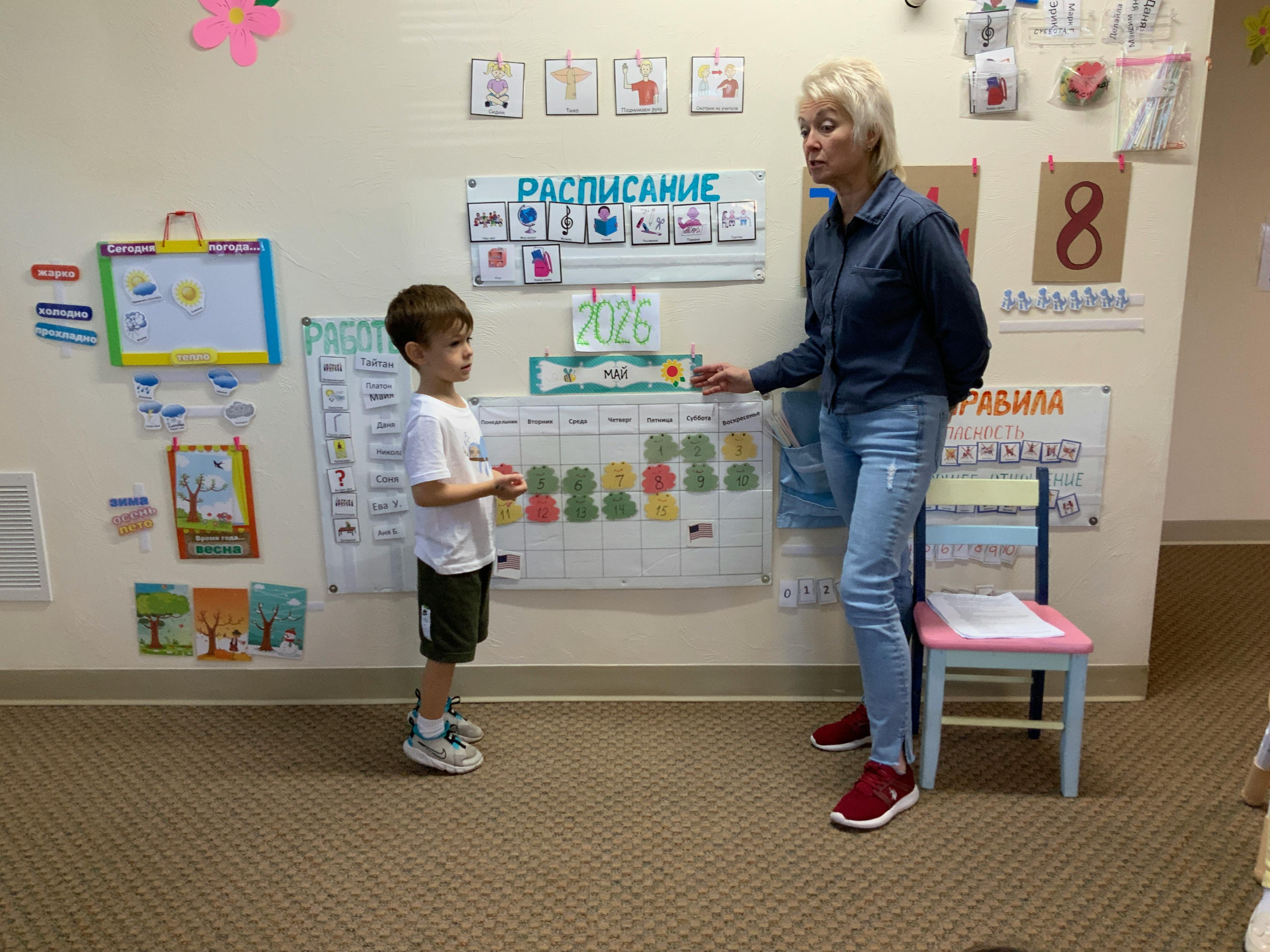 Adult and child in a classroom looking at a calendar with Russian text