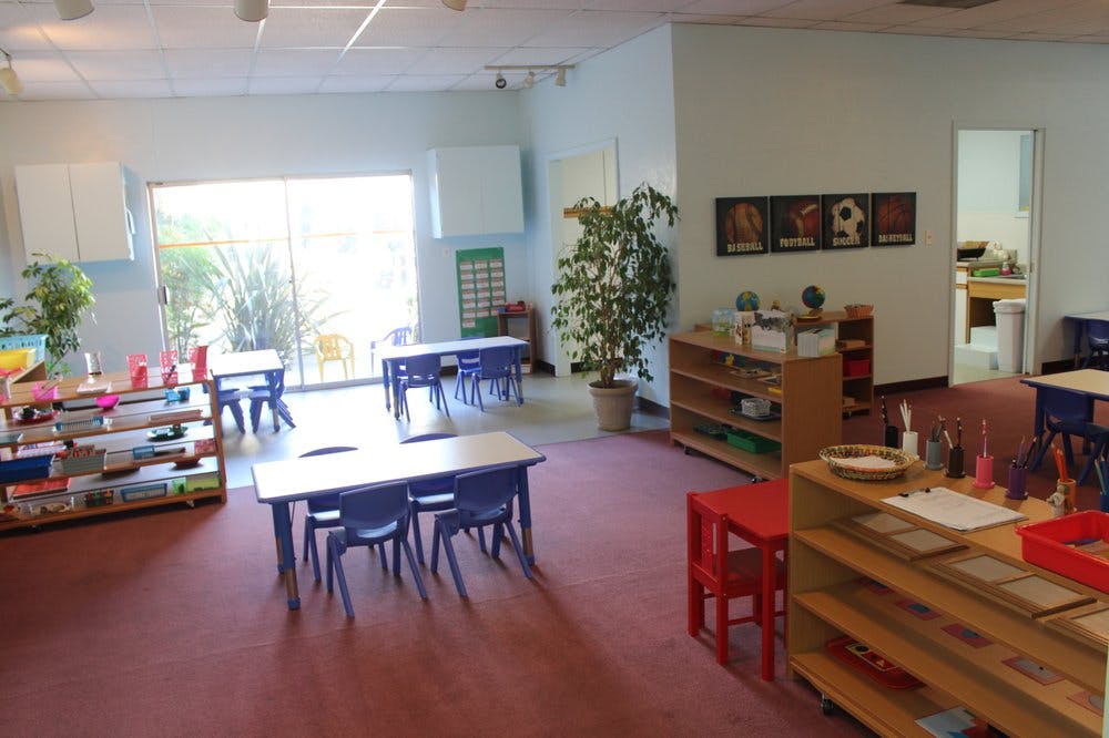 Classroom with small tables and chairs, shelves with books and materials