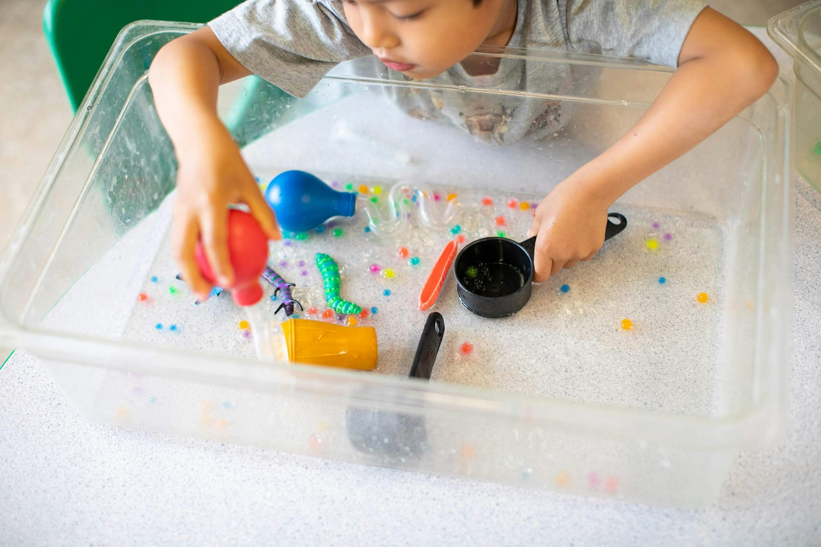 Child playing with water beads and toys in a clear bin