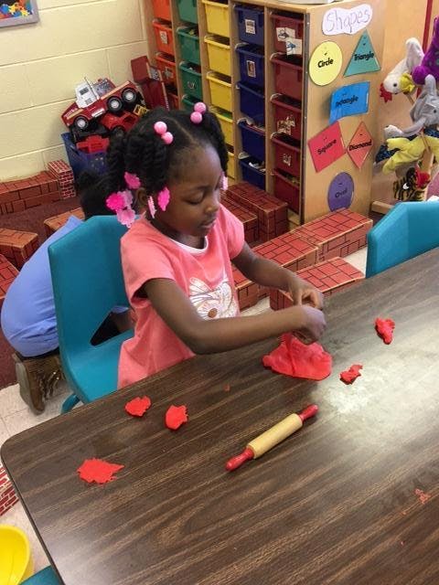 Child playing with red playdough at a table in a classroom
