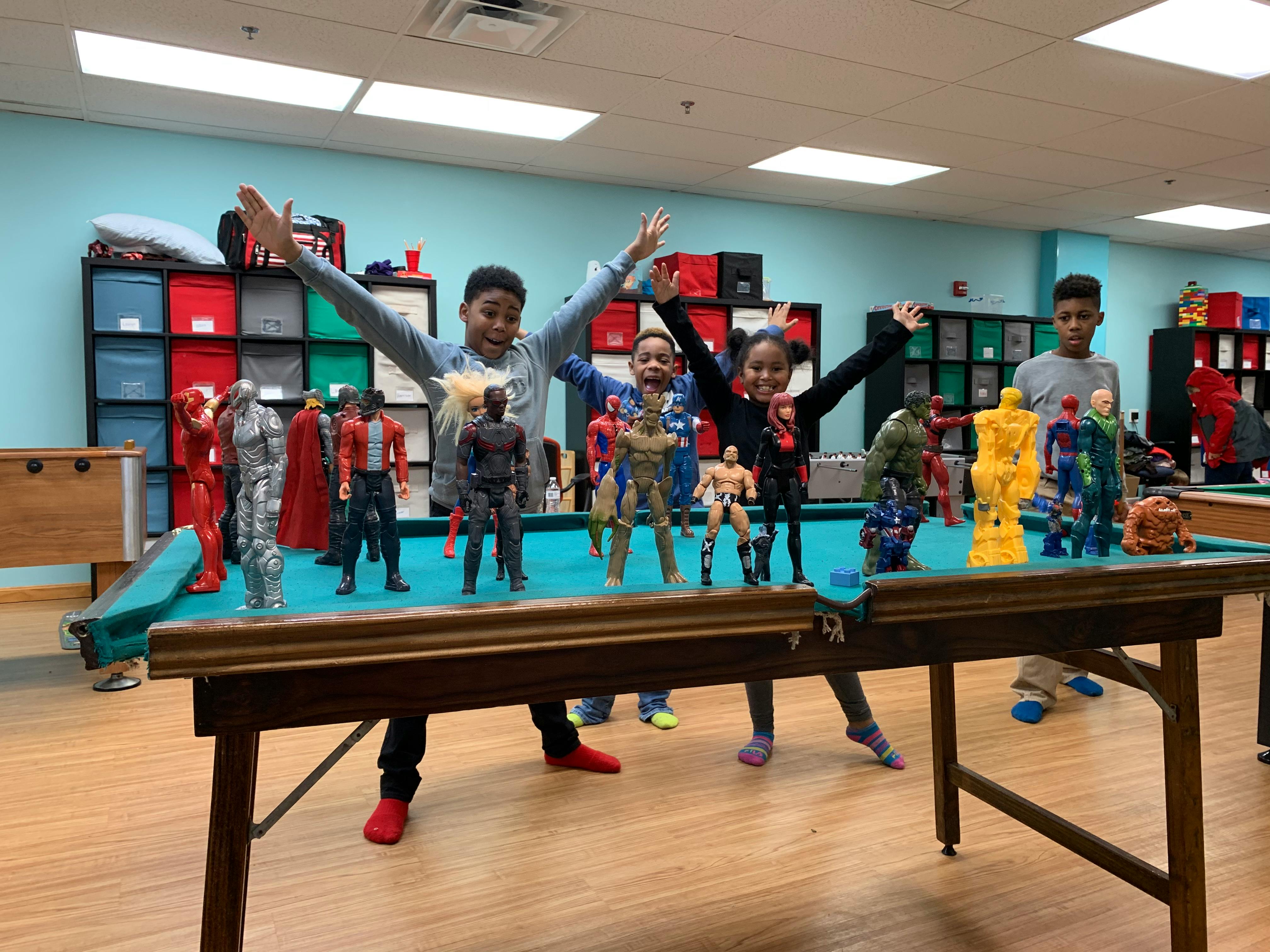 Children standing around a pool table with action figures