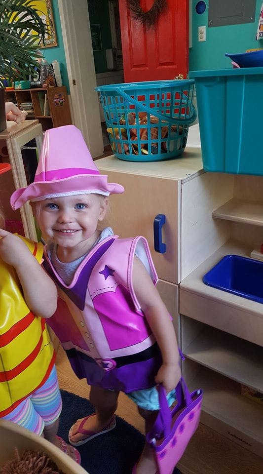 Child in a pink hat and costume holding a purple bag