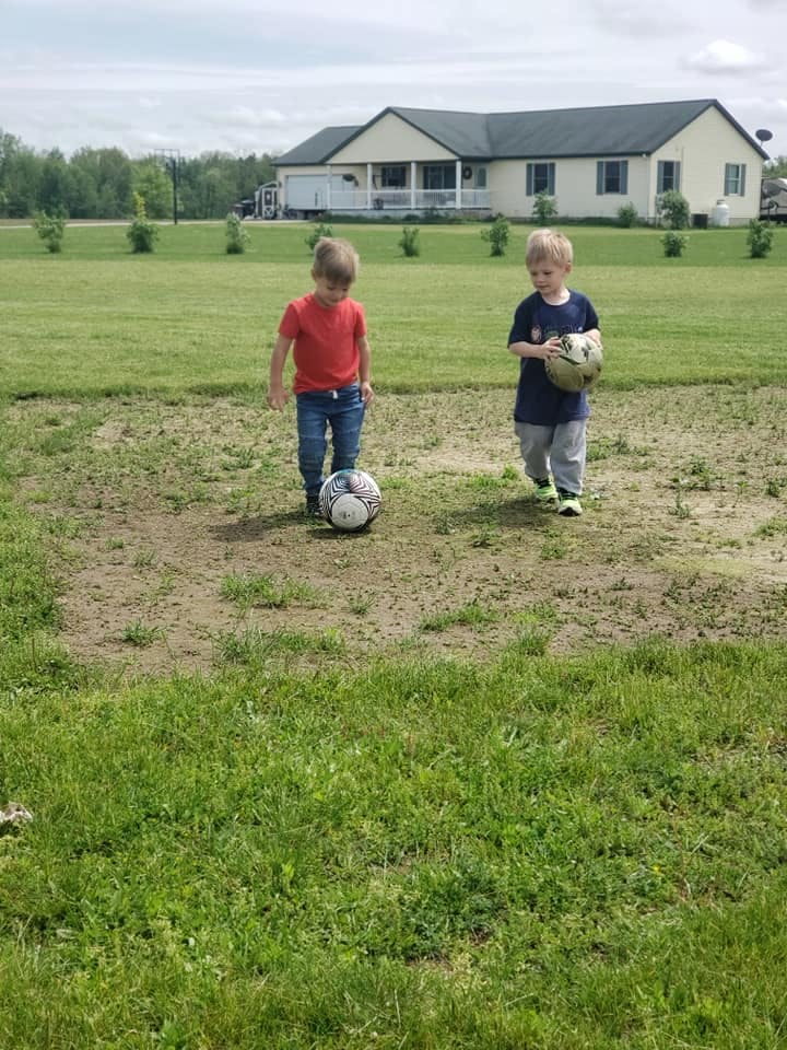 Two children playing with soccer balls in a grassy field