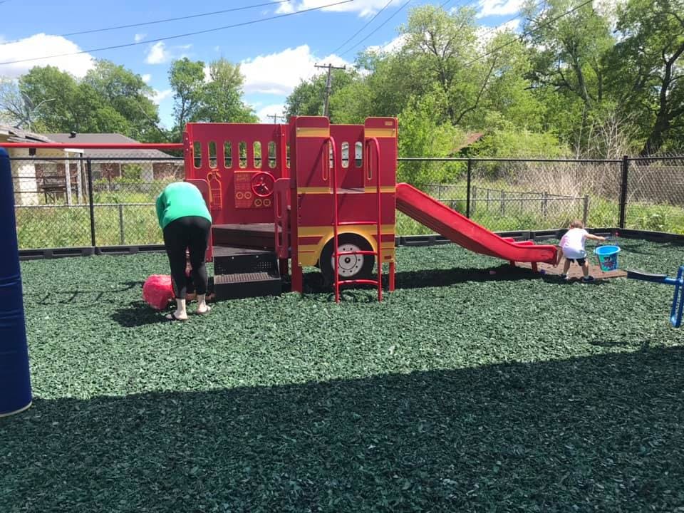 Person bending over a red ball on a playground with a child near a slide