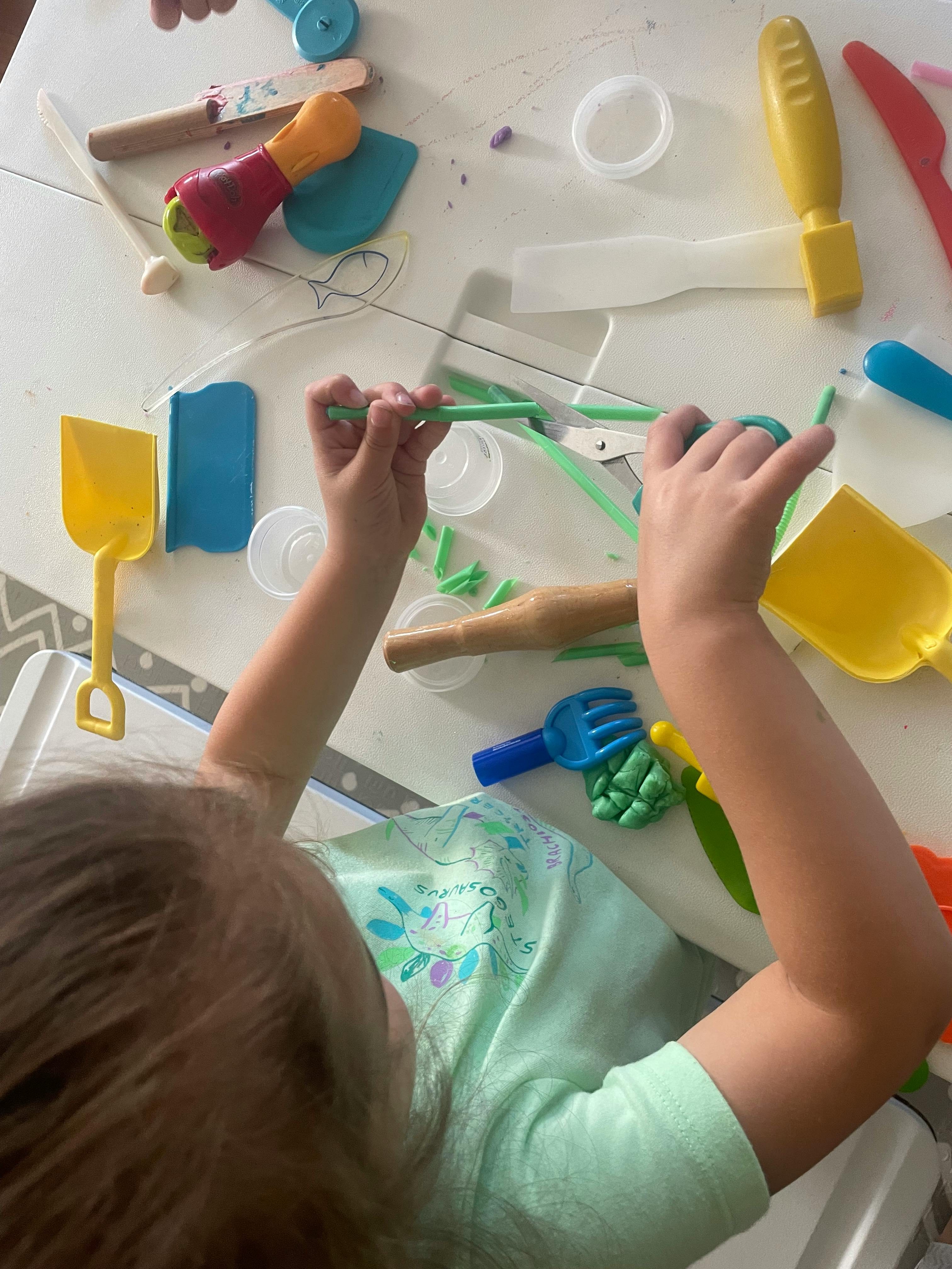 Child playing with various colorful playdough tools on a white table