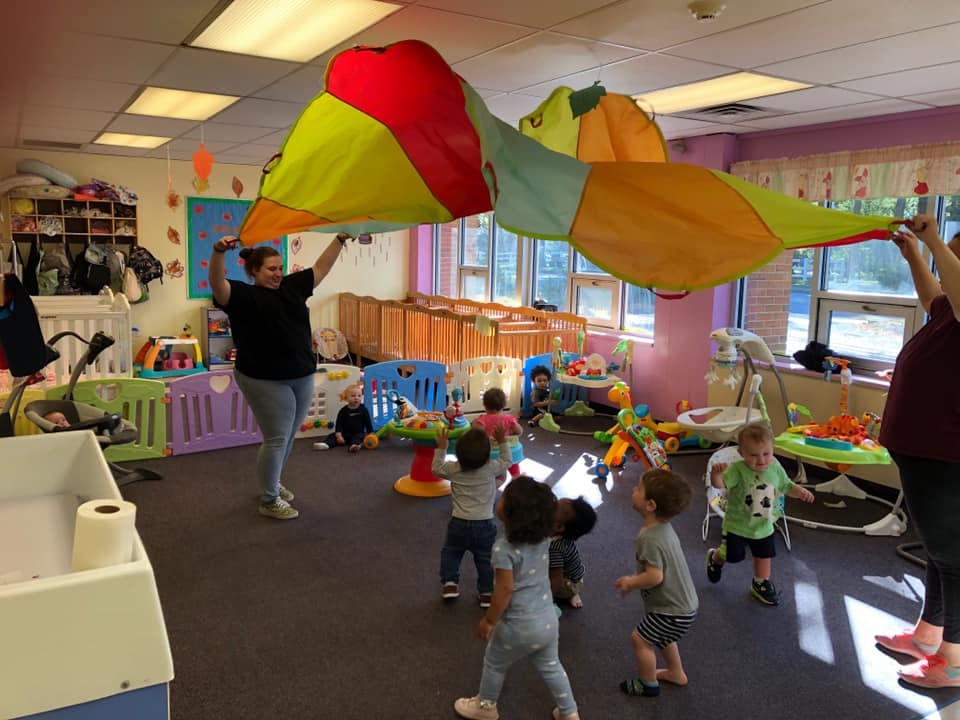 Adults and children playing with a colorful parachute in a room