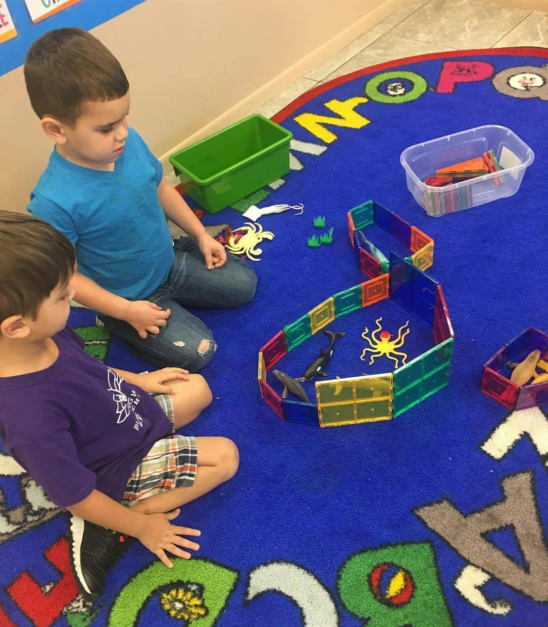 Two children playing with magnetic tiles and toys on a rug