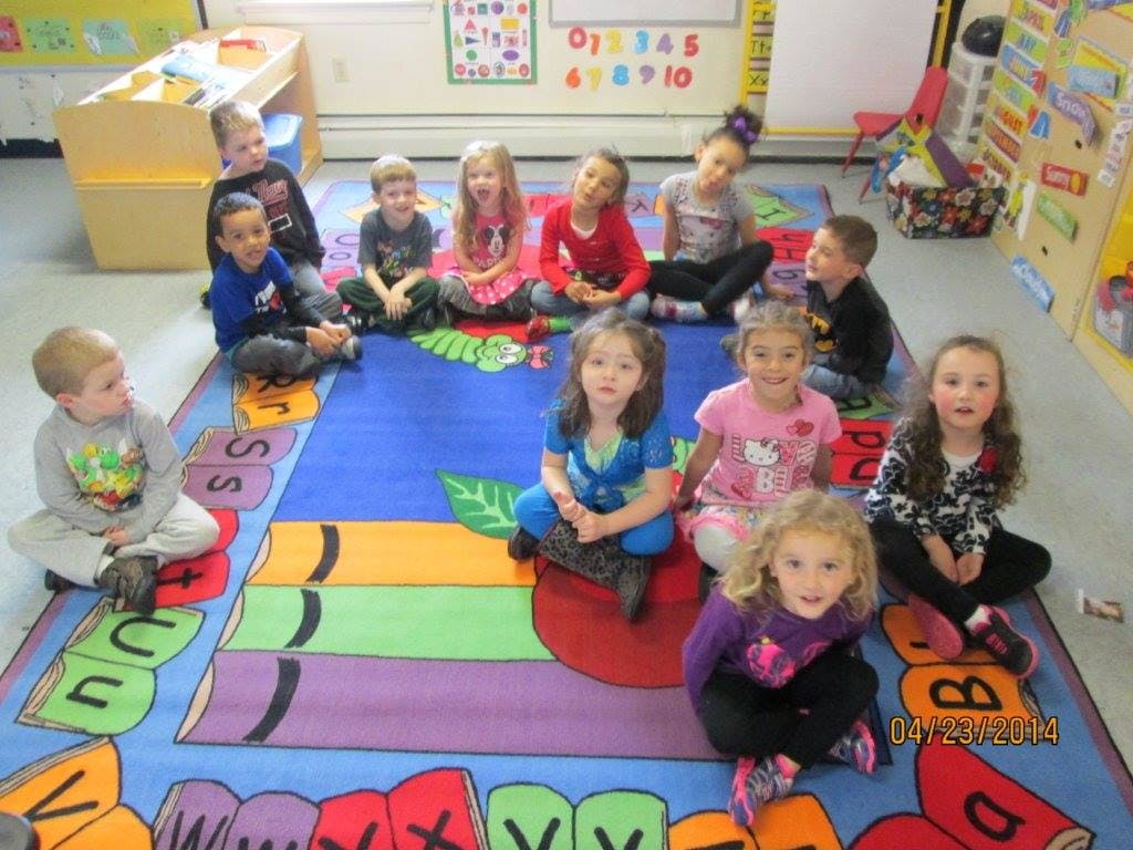 Group of children sitting on a colorful rug in a classroom