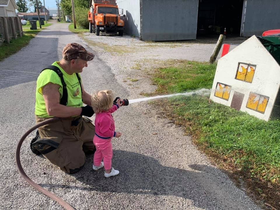 Person and child spraying water from a hose at a small playhouse