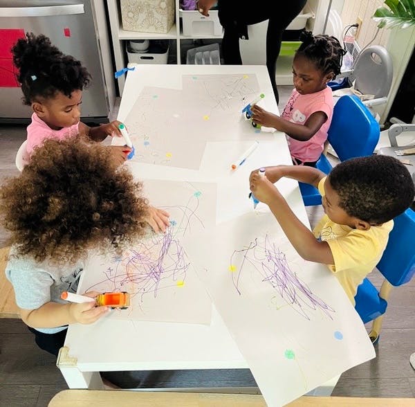 Four children drawing on paper at a table