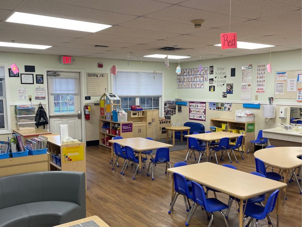 Empty classroom with small tables, blue chairs, and play kitchen