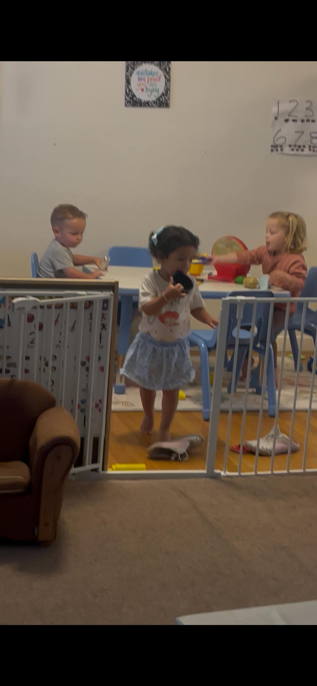 Three children playing in a room with a table and safety gate