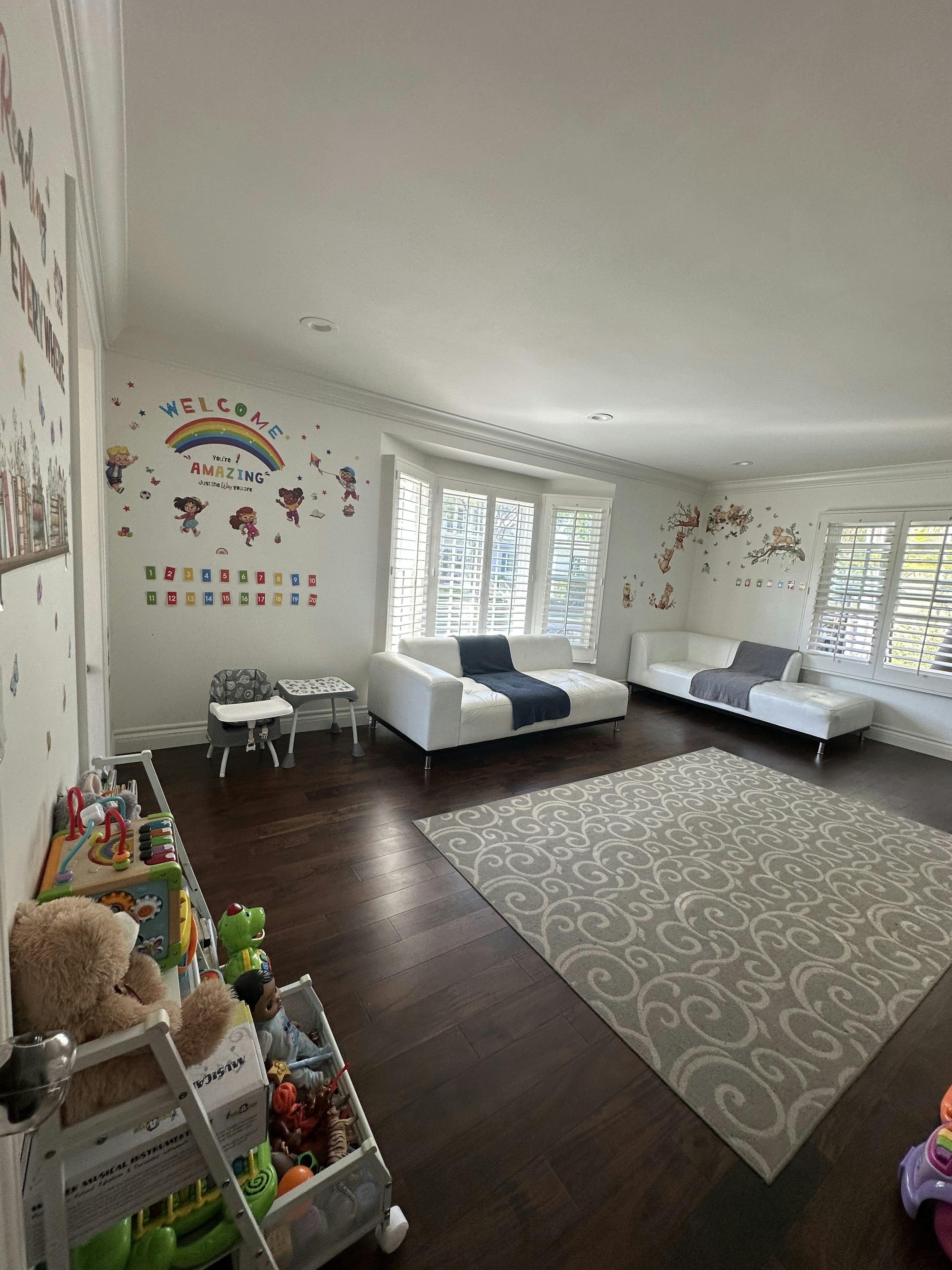 Playroom with white sofas, toys on shelves, and rainbow wall decals