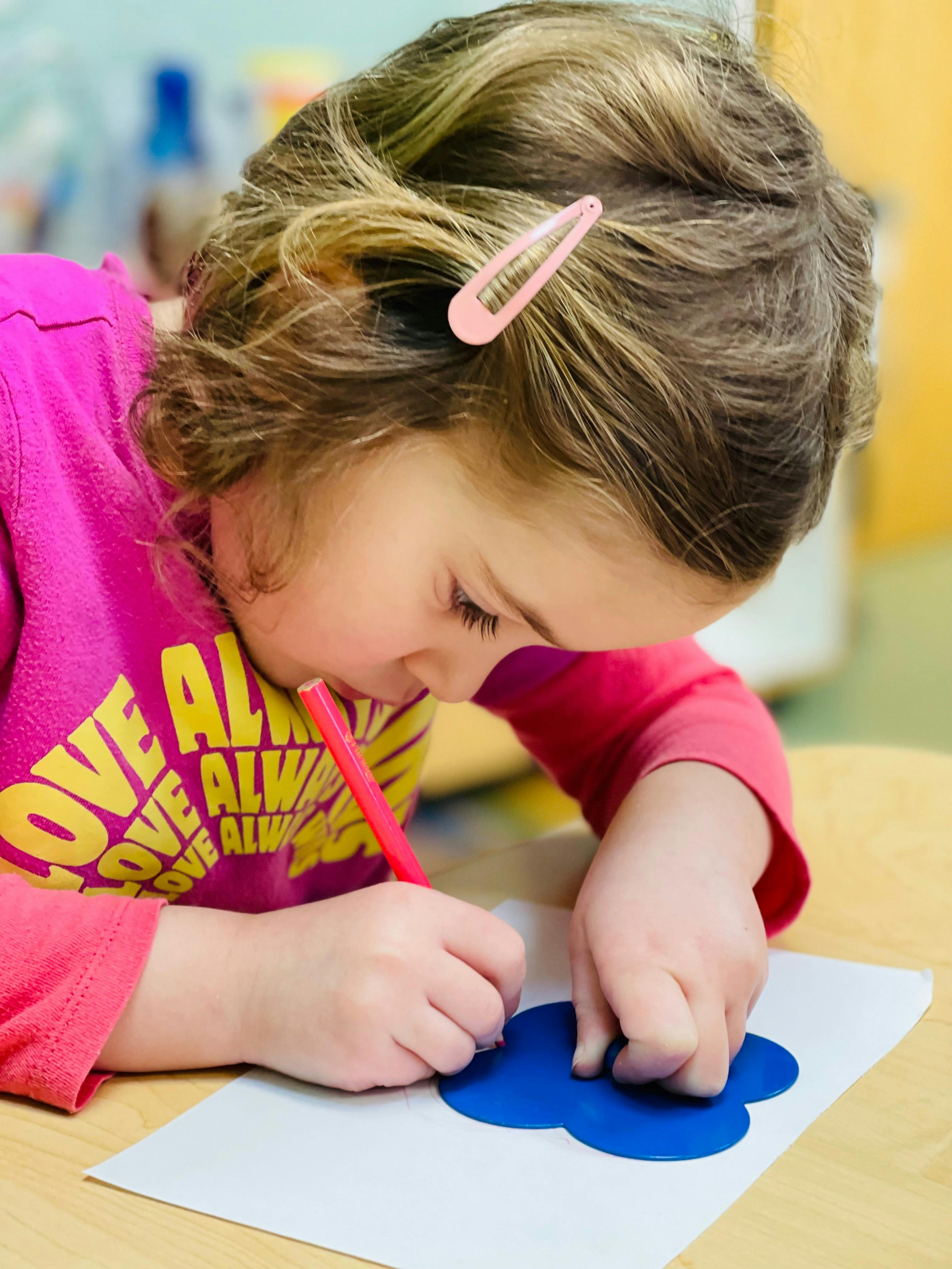 Child drawing on paper with a red crayon