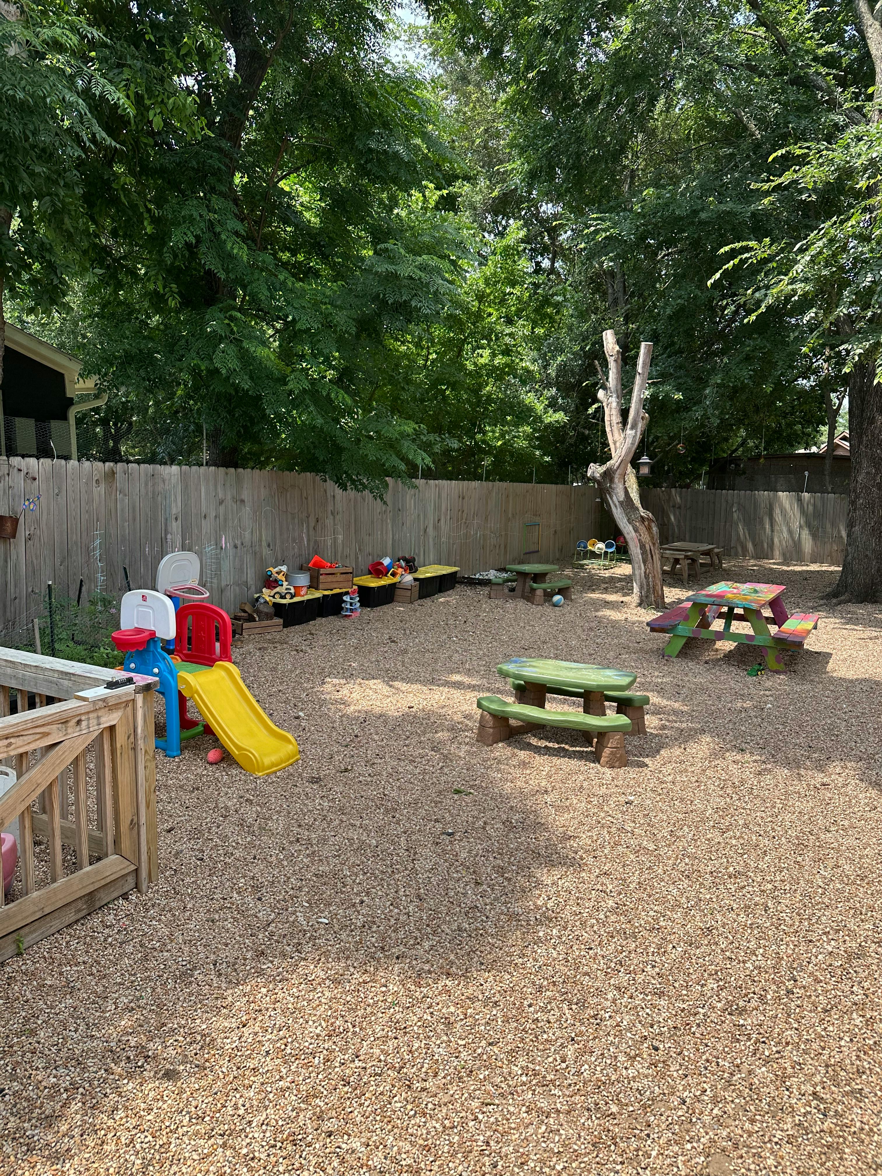 Outdoor playground with a yellow slide, picnic tables, and wood chips on the ground
