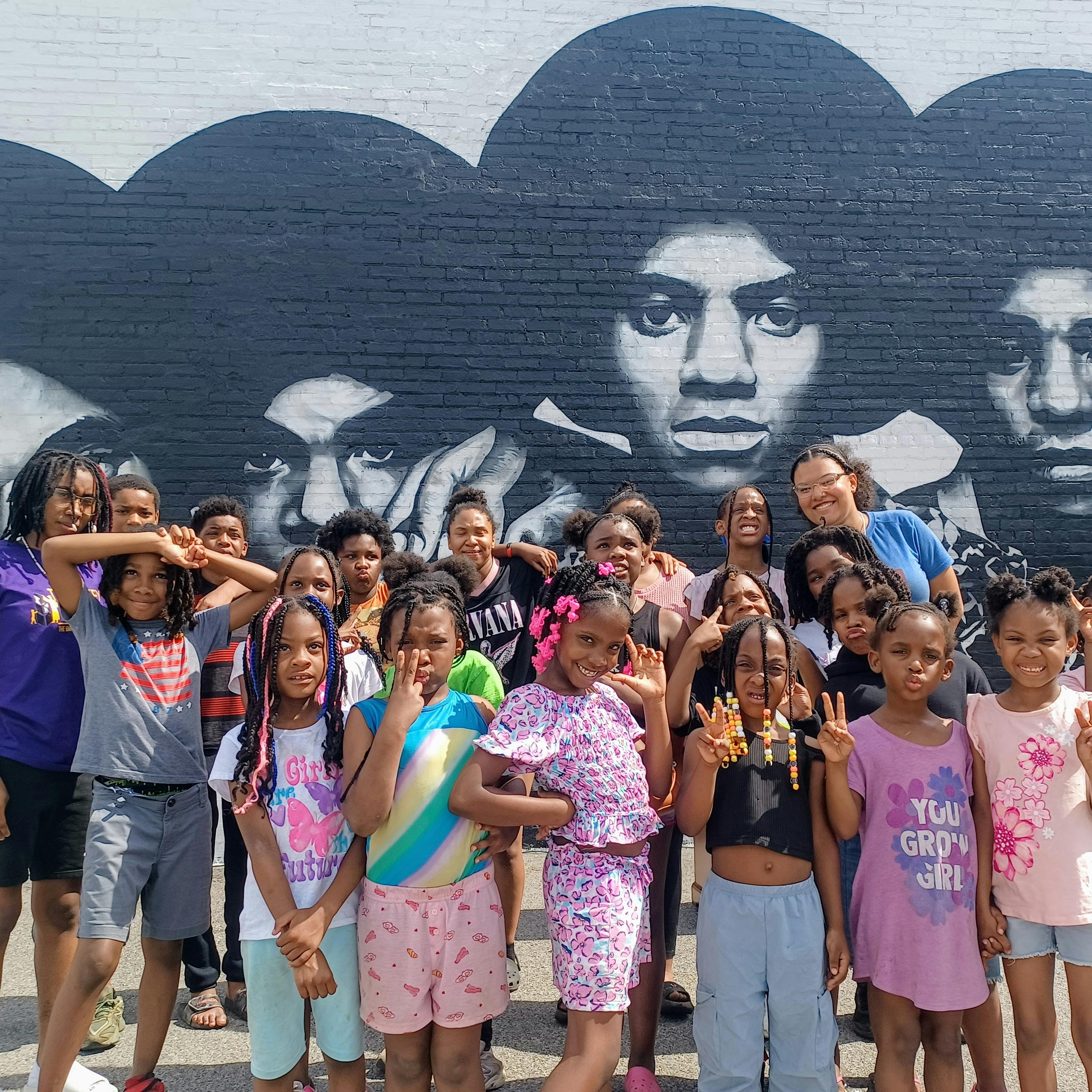 Group of children and adults standing in front of a mural