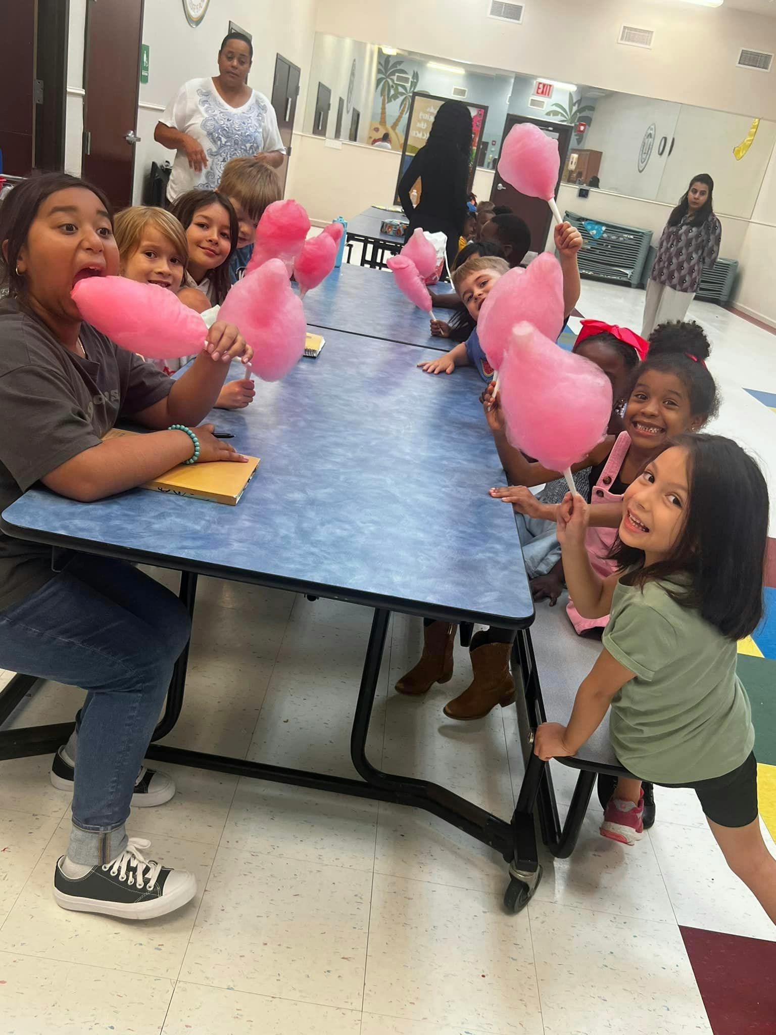 Children sitting at a table eating pink cotton candy