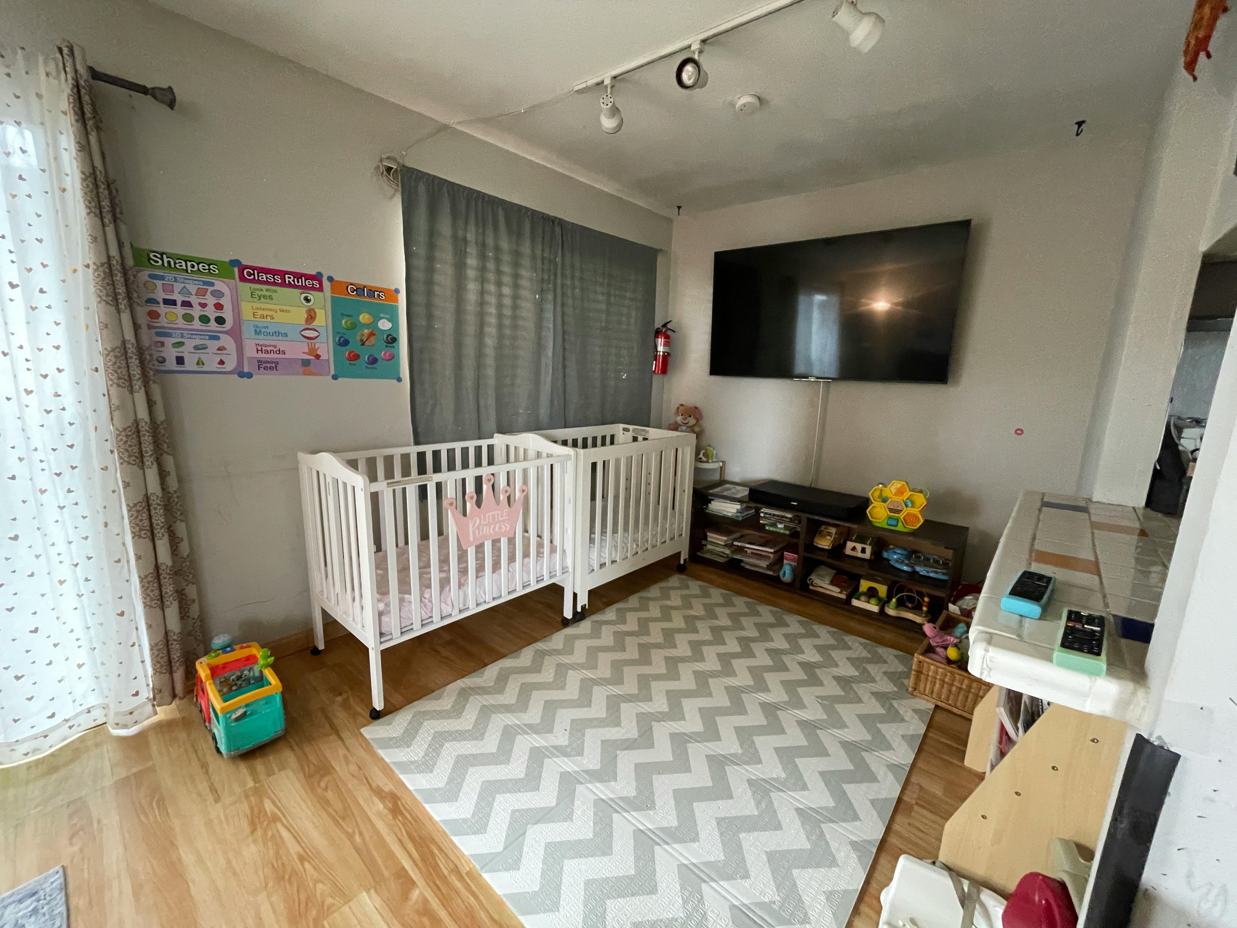 Two white cribs in a room with a chevron rug and a television