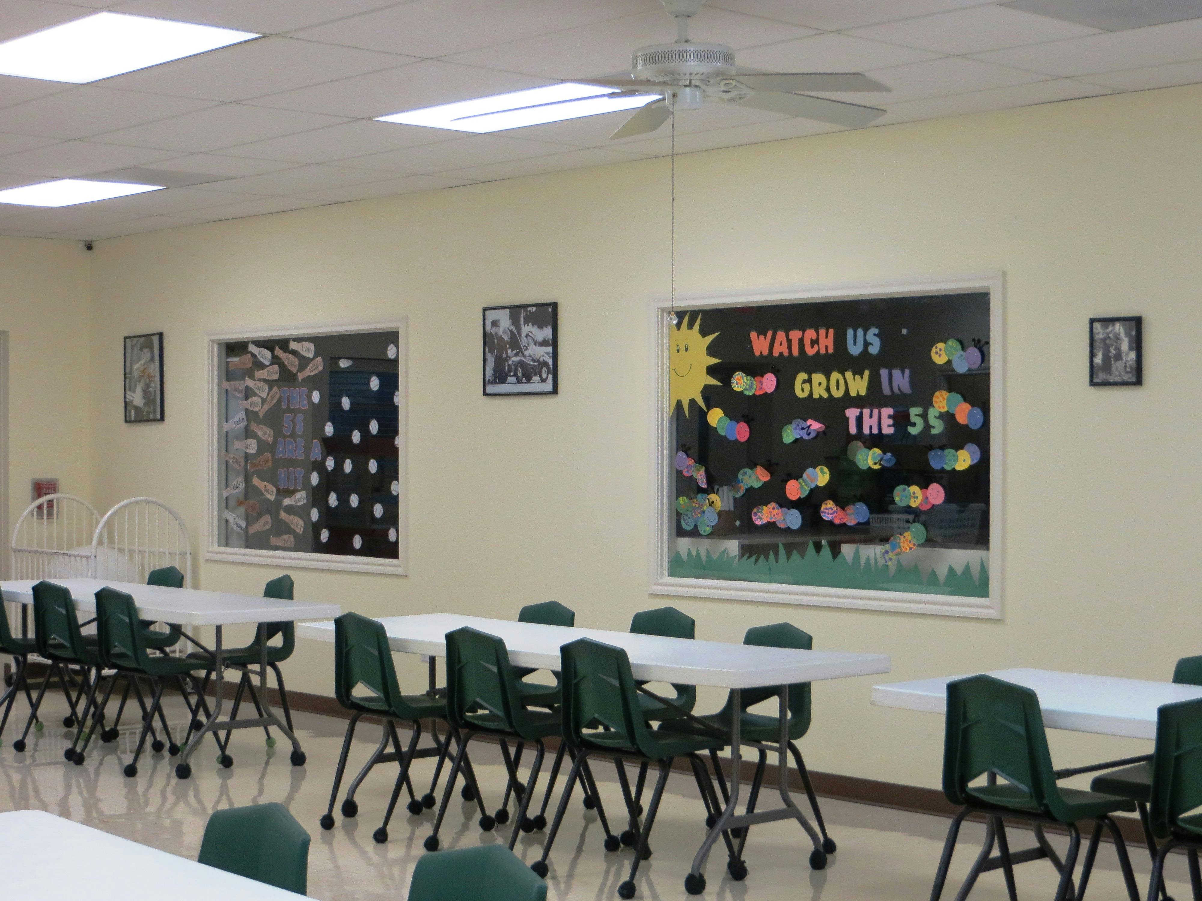 Empty classroom with tables and chairs, bulletin board with "Watch Us Grow"