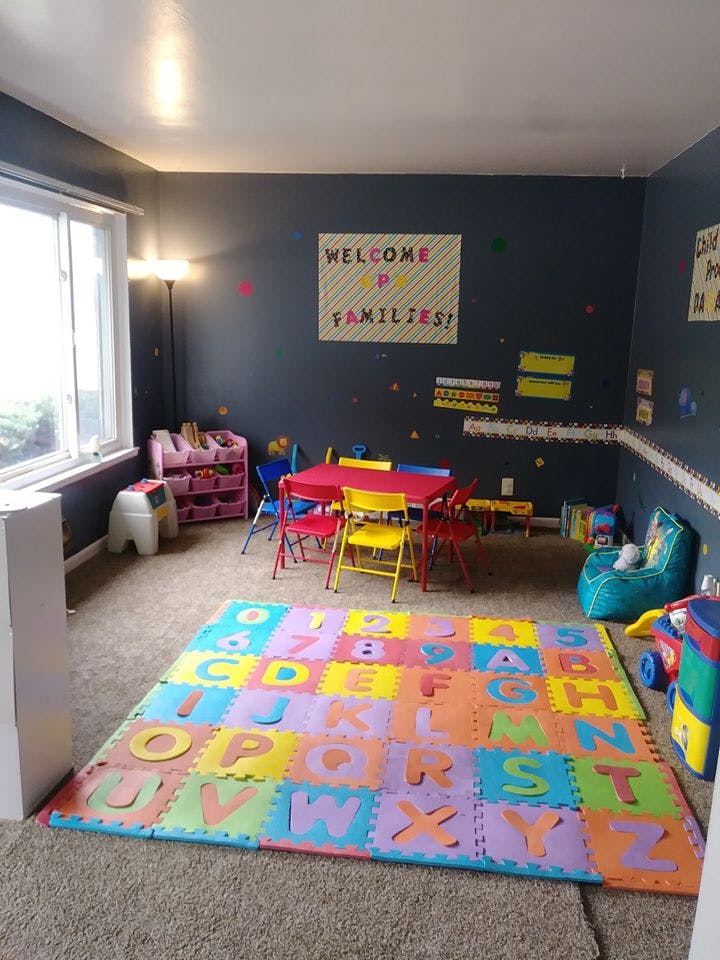 Playroom with alphabet mat, small table and chairs, and "Welcome Families" sign