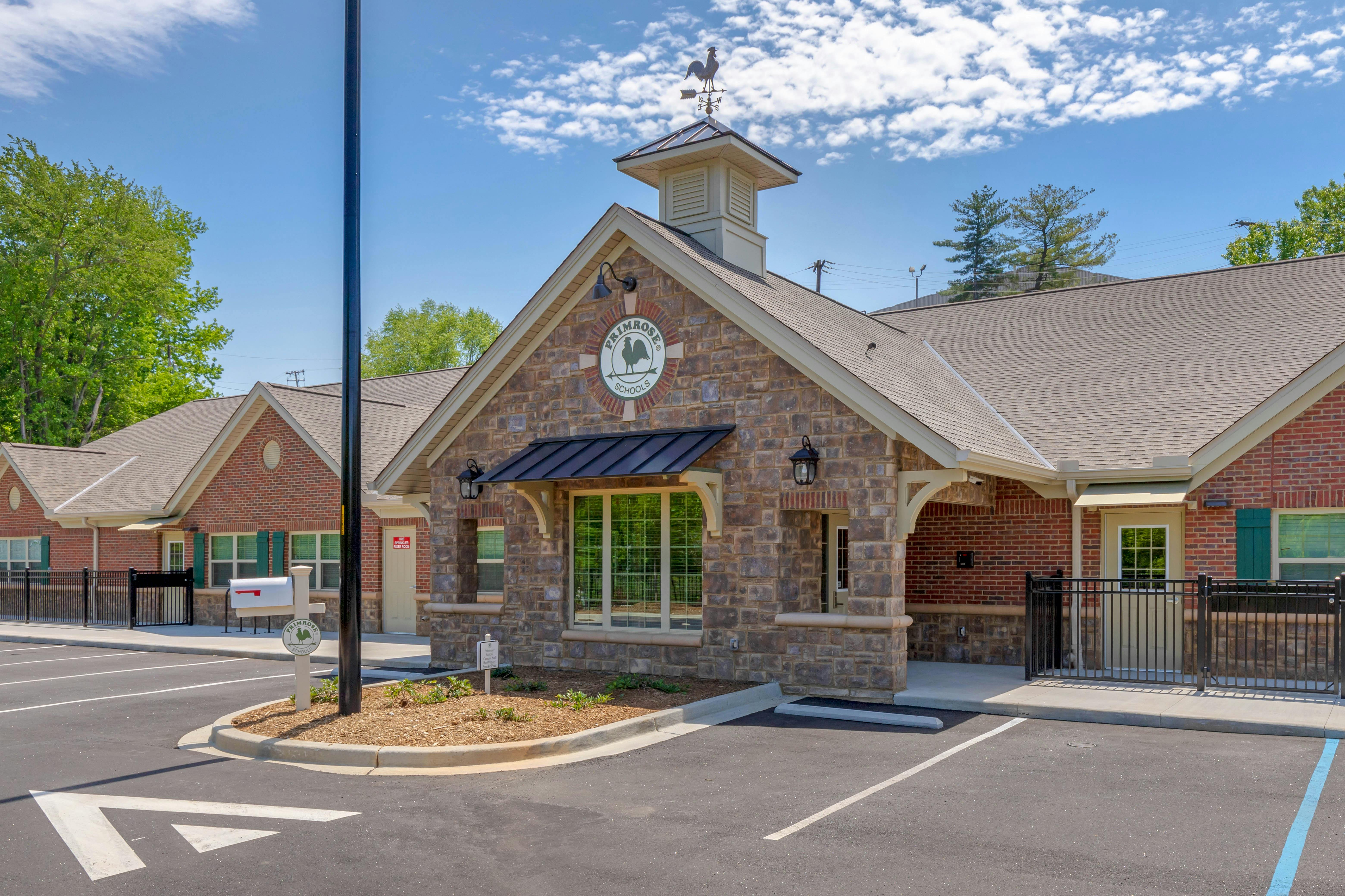 A school building with a stone facade, a cupola with a weathervane, and a Primrose Schools sign